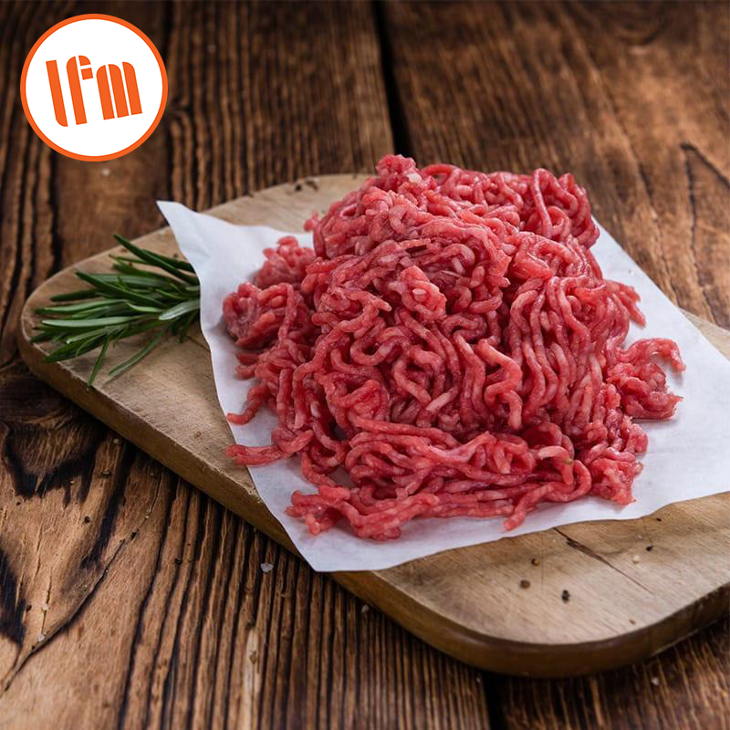 A pile of fresh ground beef on a wooden cutting board with a sprig of rosemary, placed on a wooden surface.