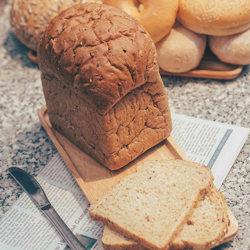Loaf of multigrain bread with a golden-brown crust, topped with a mix of seeds, displayed on a wooden cutting board.
