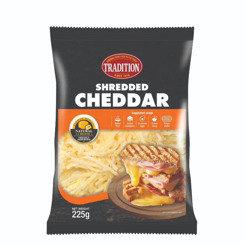 "Pack of Tradition Shredded Cheddar Cheese, 225 g – black and orange packaging featuring the brand logo 'TRADITION' at the top, big bold text reading 'SHREDDED CHEDDAR,' a window showing light-yellow shredded cheddar inside, and a grilled ham-and-cheese sandwich with melted cheddar on a wooden surface as a serving suggestion."