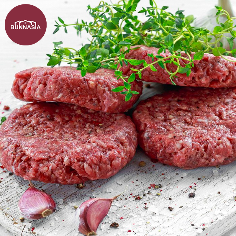 Two raw Australian lamb patties on a white surface, surrounded by onion rings and small sprigs of rosemary, with a branded logo in the top left corner.